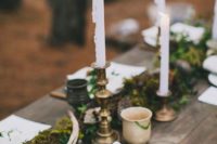 a woodland wedding table with a moss and greenery runner, antlers, moss, pinecones, candles and some nuts