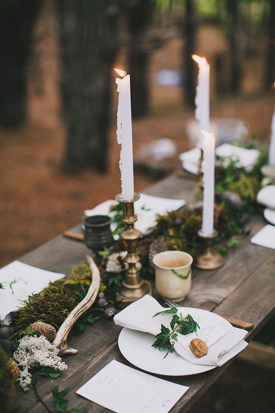 a woodland wedding table with a moss and greenery runner, antlers, moss, pinecones, candles and some nuts