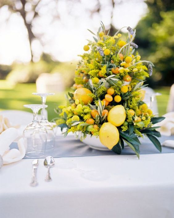 a zesty wedding centerpiece of leaves, mimosa blooms, lemons, oranges and kumquats is a gorgeous and bright piece