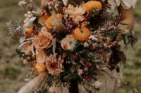 an oversized boho wedding bouquet of marigold, burgundy blooms, lots of berries, greenery and twigs