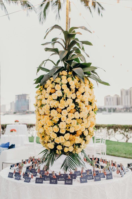 an oversized pineapple composed of peachy blooms and foliage marks the wedding escort cards and mini pineapples add to the decor