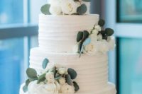 awhite textural buttercream wedding cake decorated with white blooms and greenery and with a calligraphy topper