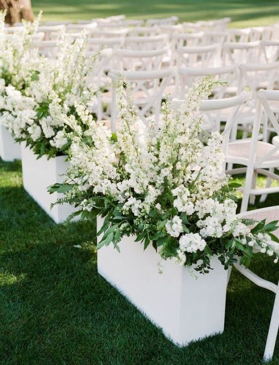 wedding ceremony space decorated with oversized white planters, greenery and white blooms for a statement