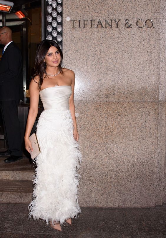 Priyanka Chopra wearing a gorgeous strapless dress with a draped top and a feather maxi skirt, blush shoes and a clutch and a diamond necklace