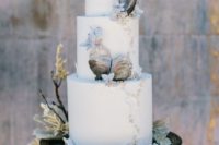 a beach wedding cake decorated with gold beads, seashells, blue blooms and blue ombre looks ethereal