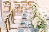 a beach wedding reception table done with a blue runner and napkins, with neutral blooms and greenery and simple cutlery