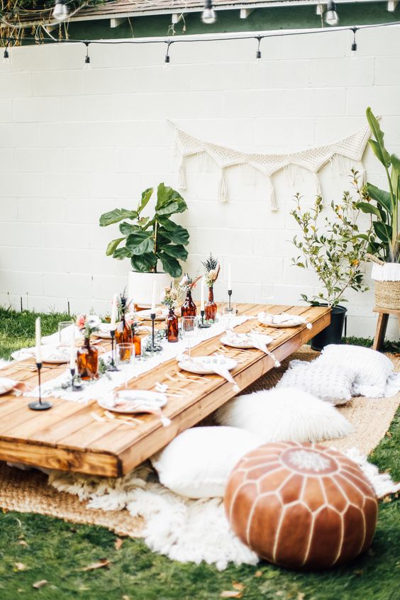 a boho summer bridal shower as a picnic with a low table, pillows and ottomans, greenery and candles