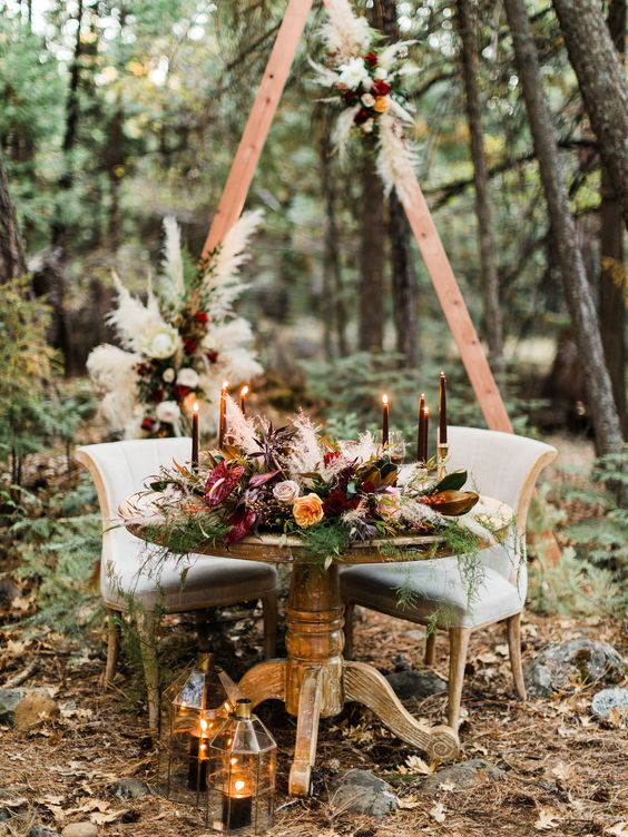 a boho woodland reception space with lush greenery, pampas grass, black candles, candle lanterns and berries is very exquisite