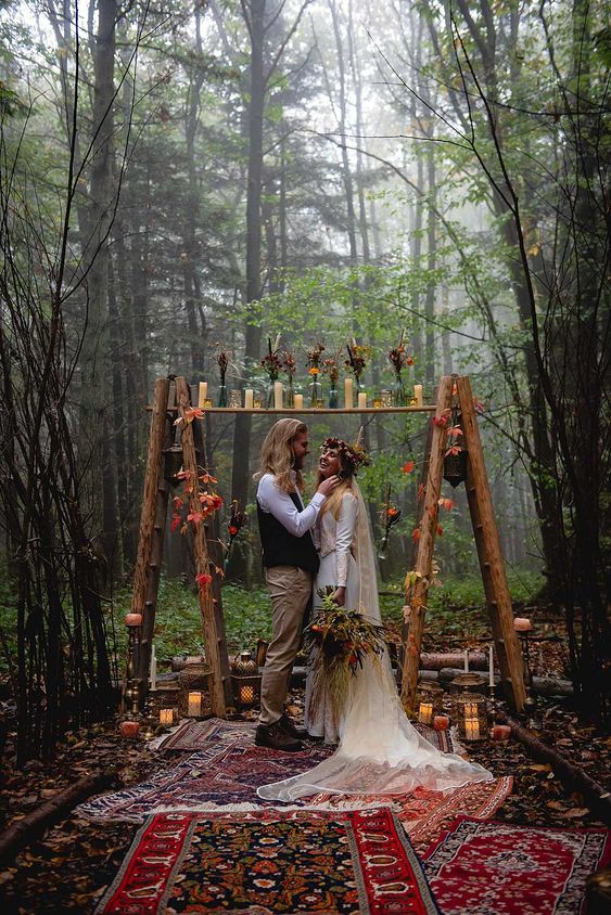 a boho woodland wedding altar of ladders, fall blooms and leaves, candles and boho rugs looks spectacular
