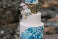 a bold blue wedding cake with a print and brushstrokes, with blooms and a candle lantern in its center