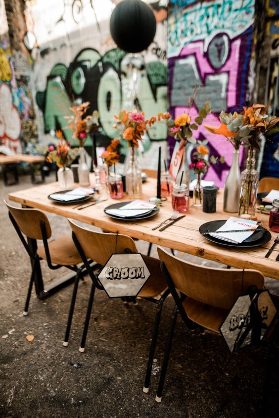a bold graffiti wedding reception space with colorful walls, with black balloons, a stained dining set with black plates and colorful blooms