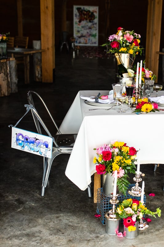 a bright wedding reception space with bold blooms, greenery, graffiti signs and with tall and thin candles