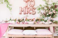 a chic pink bridal shower tablescape with blooms, greenery, pink pillows, pink table runner and napkins plus rose