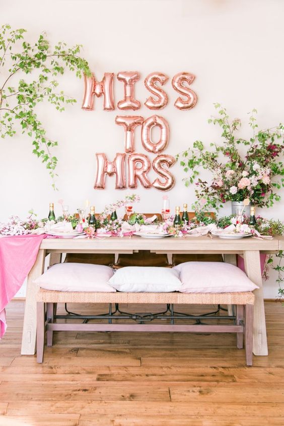 a chic pink bridal shower tablescape with blooms, greenery, pink pillows, pink table runner and napkins plus rose