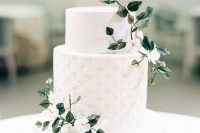 a chic white wedding cake with a plain and geometric tier, with white blooms and green leaves