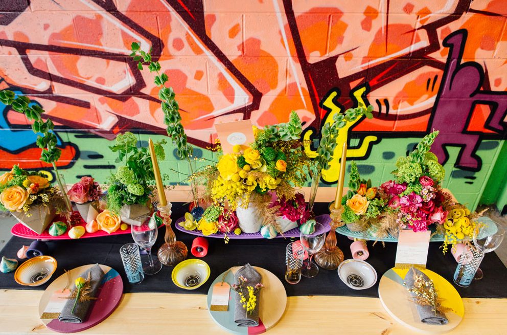 a colorful graffiti wall with bold letters and images and a bright reception table with colorful blooms, plates and candles