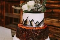 a cool mountain wedding cake with a bark tier and a painted mountain one plus wildflowers and evergreens on top