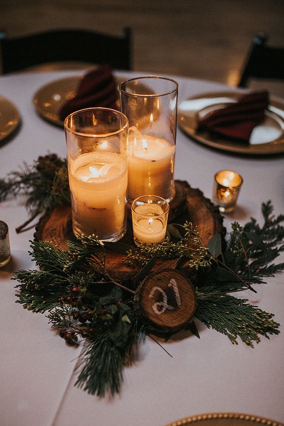 a cozy woodland wedding centerpiece of evergreens, a tree slice, candles and a tree slice table number is lovely