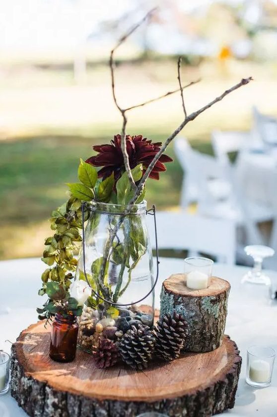 a creative fall woodland wedding centerpiece of a wood slice, pinecones and a small tree stump, a bright statement bloom, greenery and branches