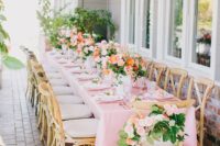 a cute and chic outdoor summer bridal shower table with pink linens, pink and peachy blooms, greenery and elegant glasses