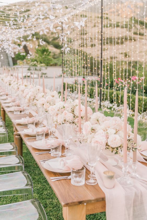 a cute and ethereal sumemr bridal shower table in blush and white, with blush candles, pastel blooms, linens and lots of lights