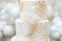 a delicate and refined white pearl wedding cake with sugar blooms and large pearls on top