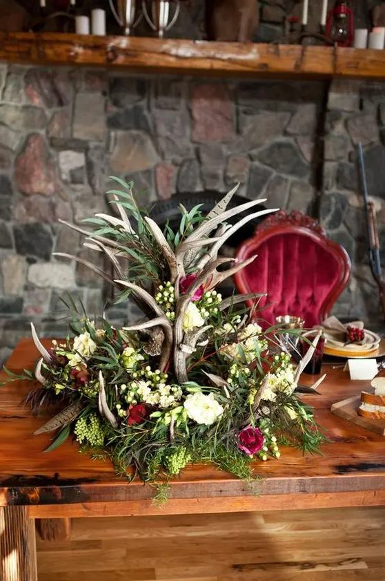 A gorgeous woodland inspired centerpiece with antlers, different blooms, greenery and feathers