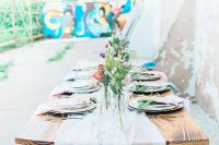 a graffiti space with bold walls and a stained table, with an airy table runner, bold blooms and greenery and shabby walls is a creative reception space
