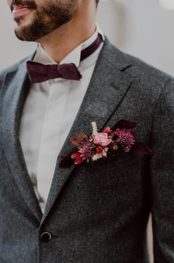 a grey tweed blazer with a bold pocket square with pink, fuchsia, deep purple blooms, feathers and berries that matches and purple bow tie