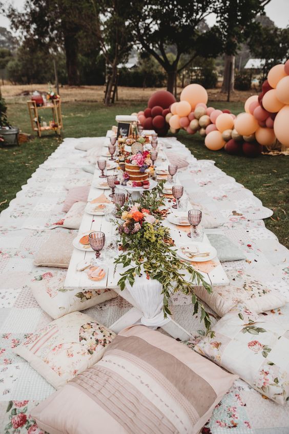 a lovely summer bridal shower picnic with a low table, printed pillows and blankets, blooms and greenery and flower topped cakes