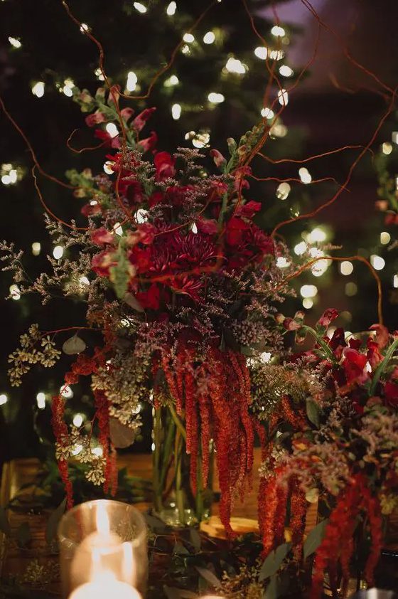 a moody forest wedding centerpiece of greenery, red blooms, amaranthus, twigs and branches is amazing