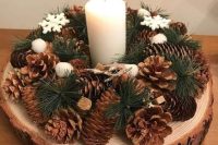 a pretty winter woodland wedding centerpiece of a tree slice, pinecones, evergreens, snowflakes and a pillar candle