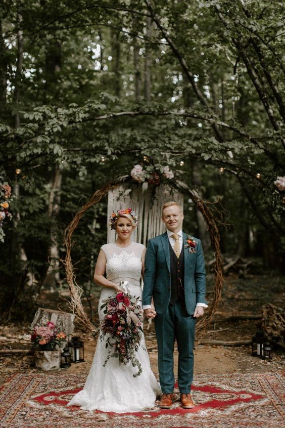 a round branch wedding arch with greenery and blooms, candle lanterns and boho rugs for a boho woodland wedding