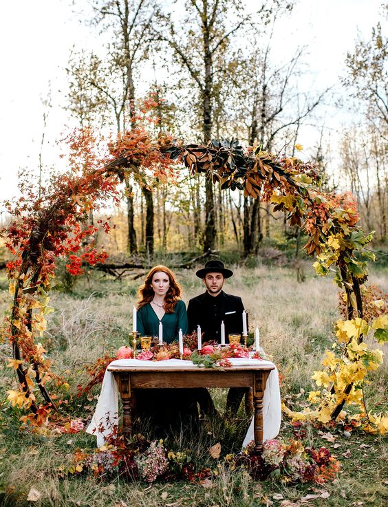 a round wedding arch covered with bright fall leaves and foliage is a cool idea for any fall woodland wedding