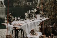 a rustic boho reception space by the lake with candles, bulbs and textural greenery decor