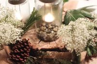 a rustic wedding centerpiece with mason jars, pebbles, a wood slice, evergreens, baby’s breath