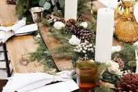 a rustic winter wedding table with evergreens, pinecones, berries, pillar candles, white blooms and greenery