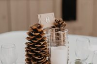 a simple and cool woodland wedding centerpiece of a tree slice, greenery and large pinecones plus a table number