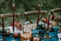 a simple fall mountain wedding tablescape with a blue runner, burgundy candles, chcked napkins and fruits on the runner