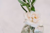 a square bottle with olive greenery and a blush rose is a romantic and cute wedding centerpiece