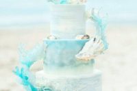 a statement beach wedding cake done with turquoise watercolors, with seashells and swirls of water made of sugar