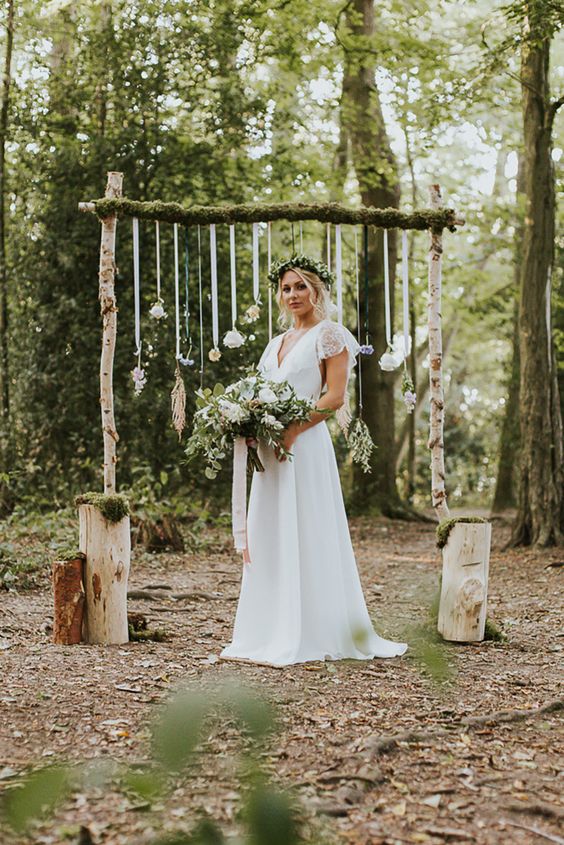 a summer woodland wedding arch of branches, ribbons with greenery and neutral blooms and stumps with moss