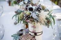 a vase wrapped with book pages, pale leaves, pinecones and textural herbs for a unique snowy-inspired centerpiece