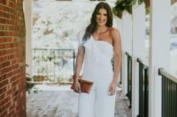 a white one shoulder ruffle strap jumpsuit with wideleg pants and a small brown leather clutch compose an elegant modern look