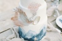 a white wedding cake with blue watercolors, corals and a seashell with pearls for a beach wedding