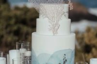a white wedding cake with blue watercolors, silver foil and corals for a blue beach wedding