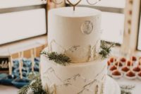 a white wedding cake with buttercream mountains and trees, evergreens and a wooden cake topper