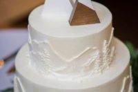 a white wedding cake with buttercream trees and mountains and cute wooden mountain toppers on it