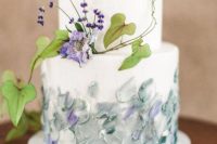 a white wedding cake with textural pastel decor and fresh purple blooms and leaves for a spring or summer wedding