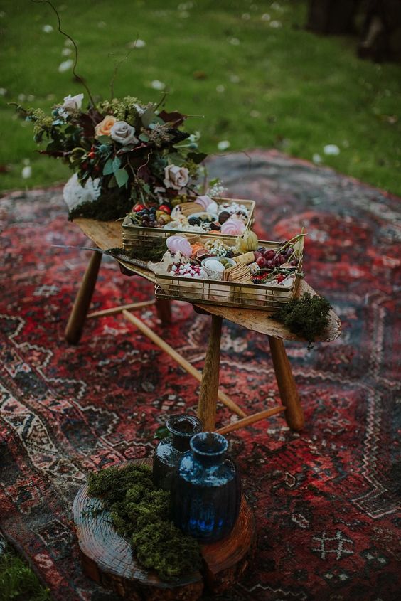 a woodland boho wedding food display of a bench with wooden crates, fruits, berries and cheeses, bold blooms and greenery is lovely